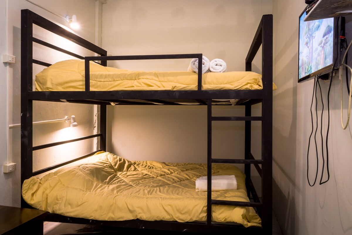 A bunk bed with yellow bedding, a TV mounted on the wall, and visible electrical outlets.
