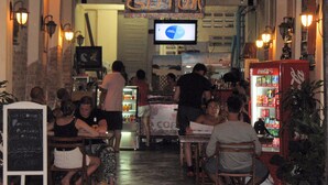 A busy indoor dining area with tables and chairs, a Coca-Cola vending machine, and a chalkboard sign. - Gotum Hostel & Restaurant (Phuket)
