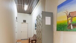 A hallway with lockers, a bench, a trash bin, and a painting on the wall. - Gotum Hostel & Restaurant (Phuket)