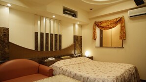 A hotel room with a bed, a chair, a small table, a mirror, and a wall-mounted air conditioner. - Hotel Olive Sakai (Sakai)