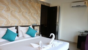 Une chambre d’hôtel avec un grand lit, une serviette en forme de cygne, des coussins de couleur turquoise et un papier peint à motifs.