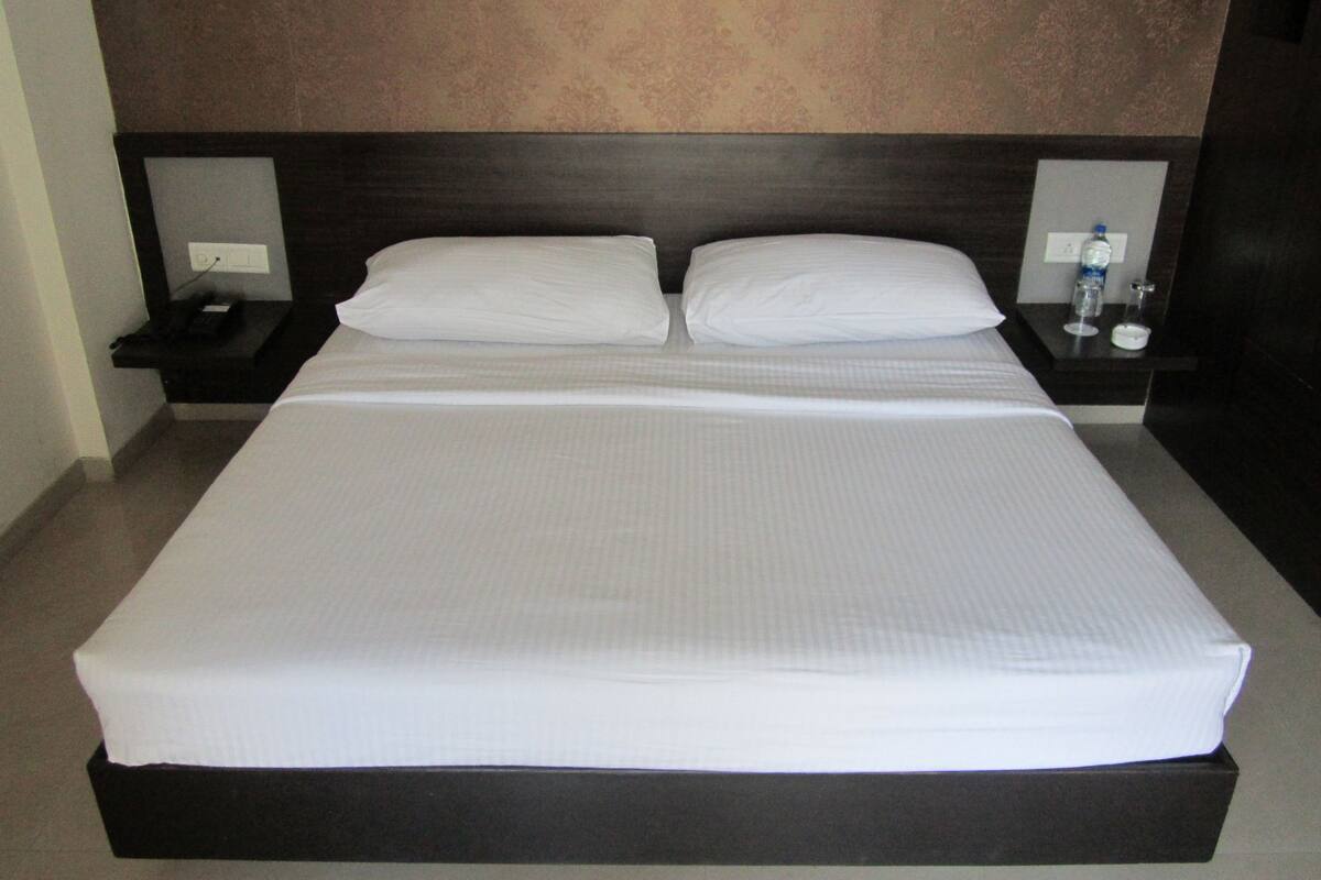 A large bed with white linens, two nightstands, and a wall-mounted lamp.