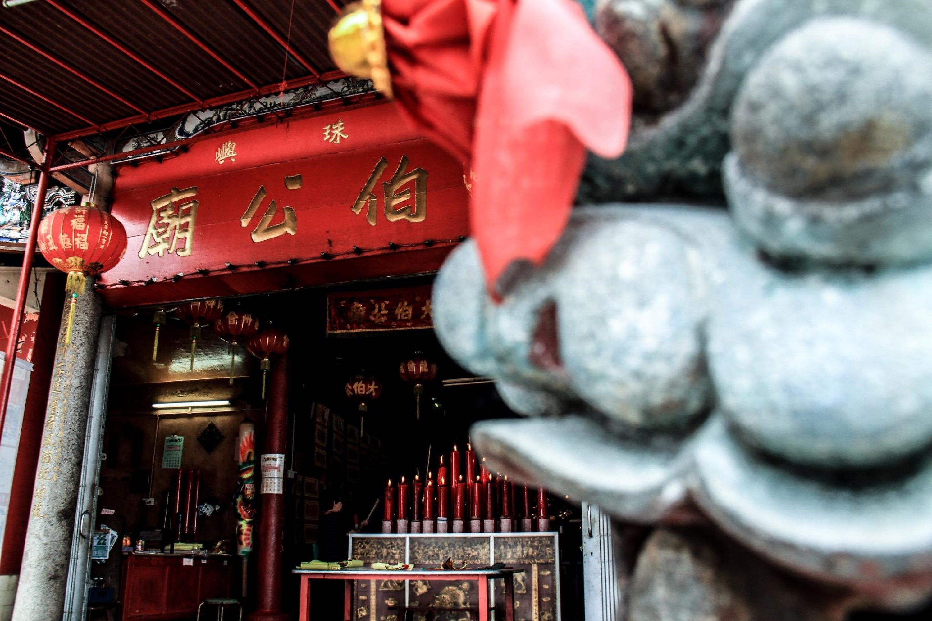 A traditional Chinese temple entrance with red decorations and a stone lion statue.