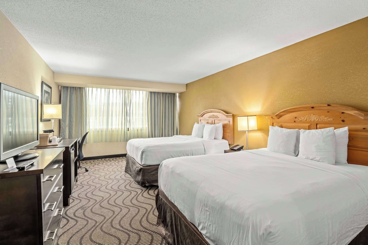 A hotel room with two beds, a desk, a TV, and a window with curtains.