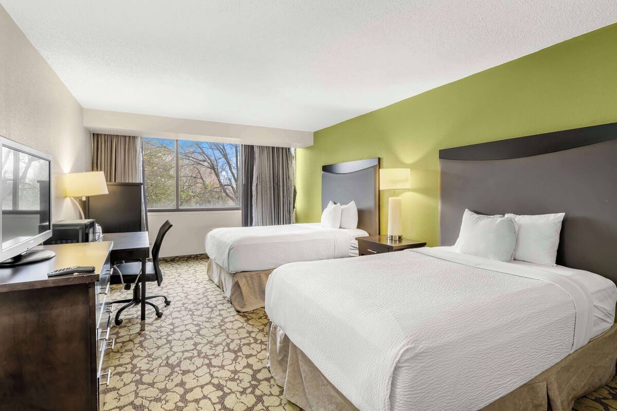 A hotel room with two beds, a desk with a computer, a chair, and a TV.
