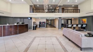 A spacious lobby with a reception desk, seating area, and a staircase leading to an upper level. - Red Lion Hotel Charlotte (Charlotte)