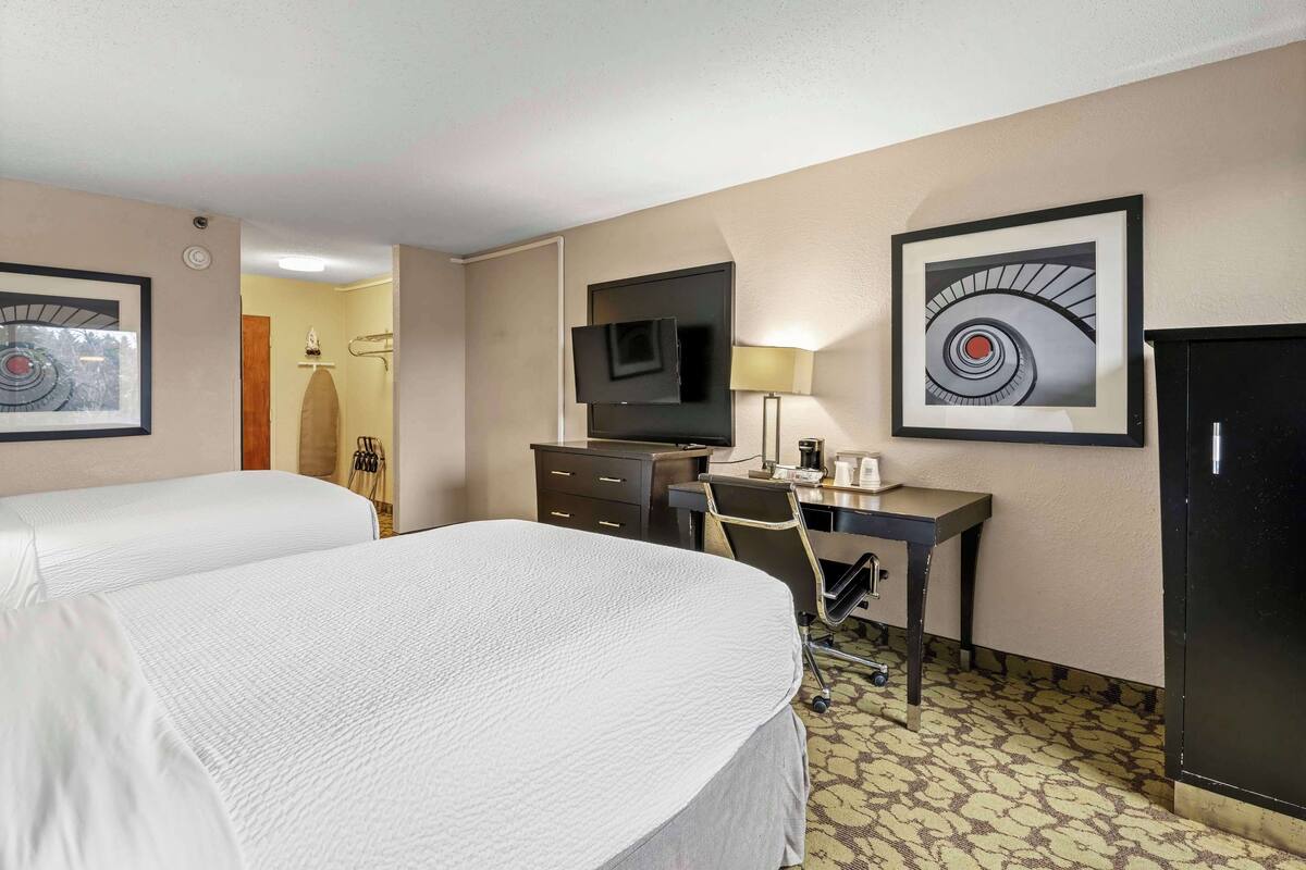 A hotel room with two beds, a desk, a TV, and artwork on the walls.