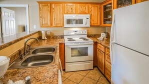 A kitchen with granite countertops, a stainless steel sink, a white stove, and wooden cabinets. - The Townhouses (Branson)