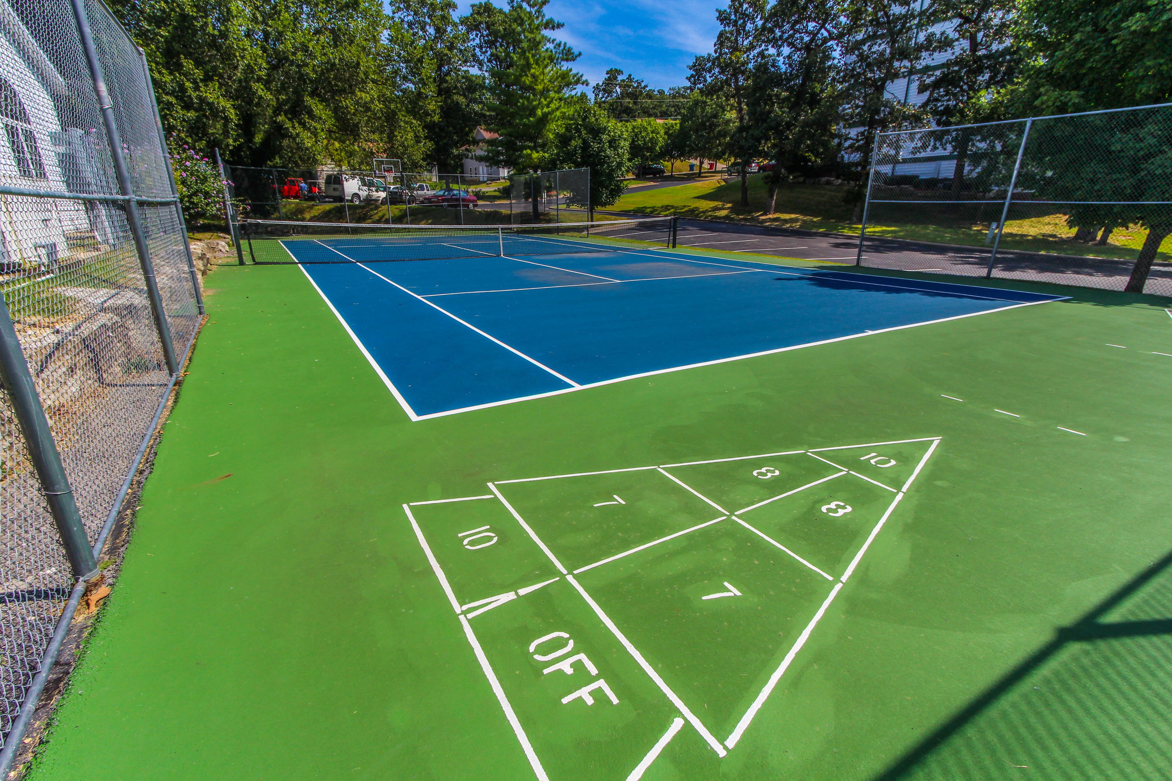 Un court de tennis doté d’une surface verte et de lignes de démarcation blanches, entouré d’une clôture en treillis métallique.