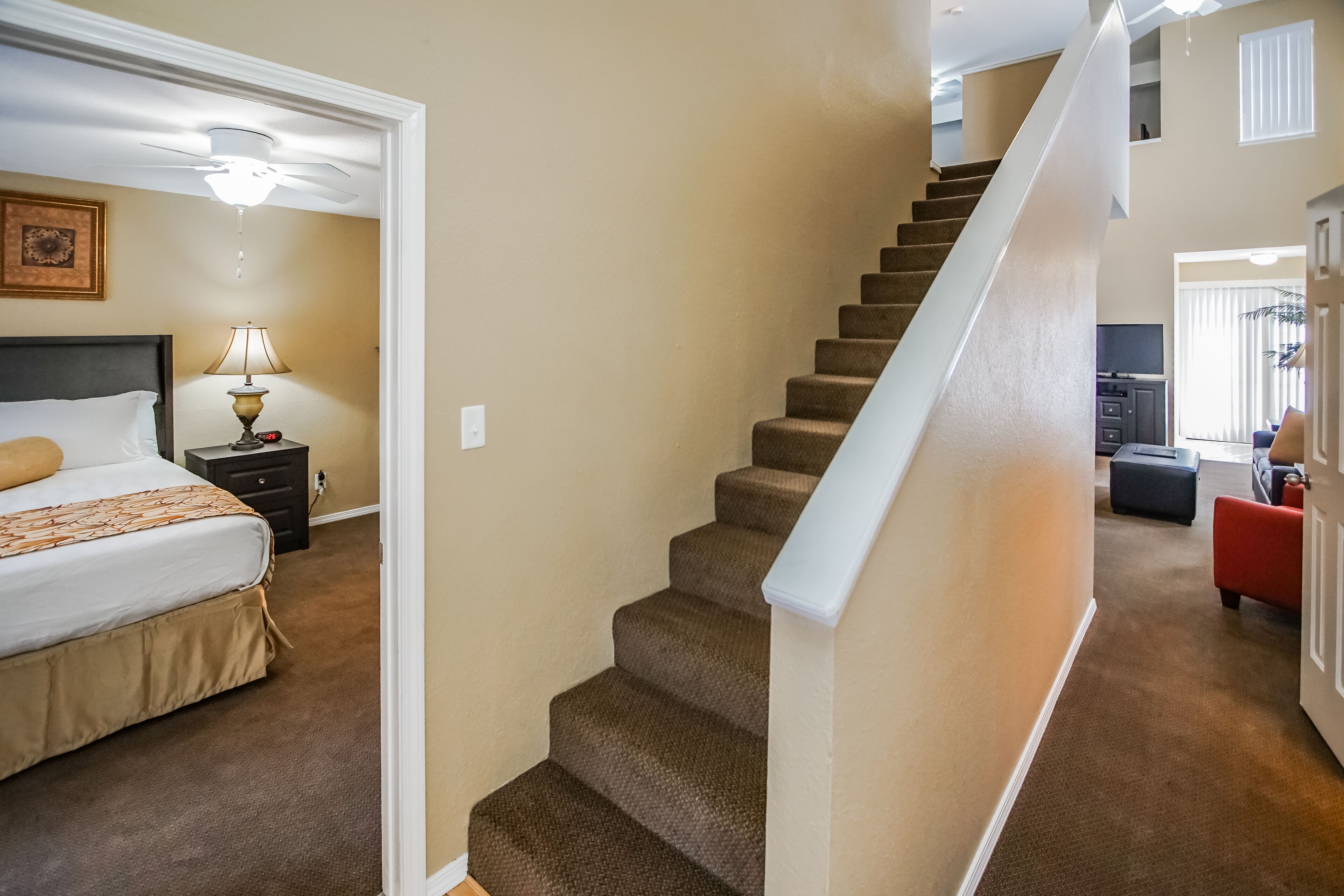 A bedroom with a bed, nightstand, lamp, and a staircase leading to a living area.