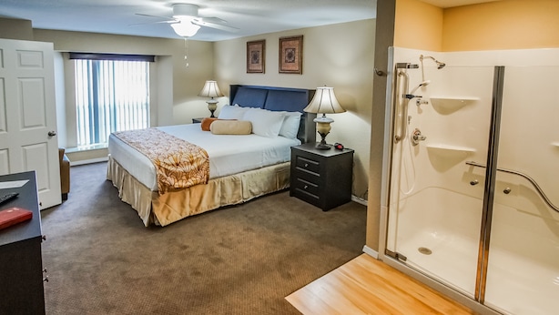 A hotel room with a bed, bedside tables, a desk, a wardrobe, a shower, and a window with blinds. - The Townhouses (Branson)