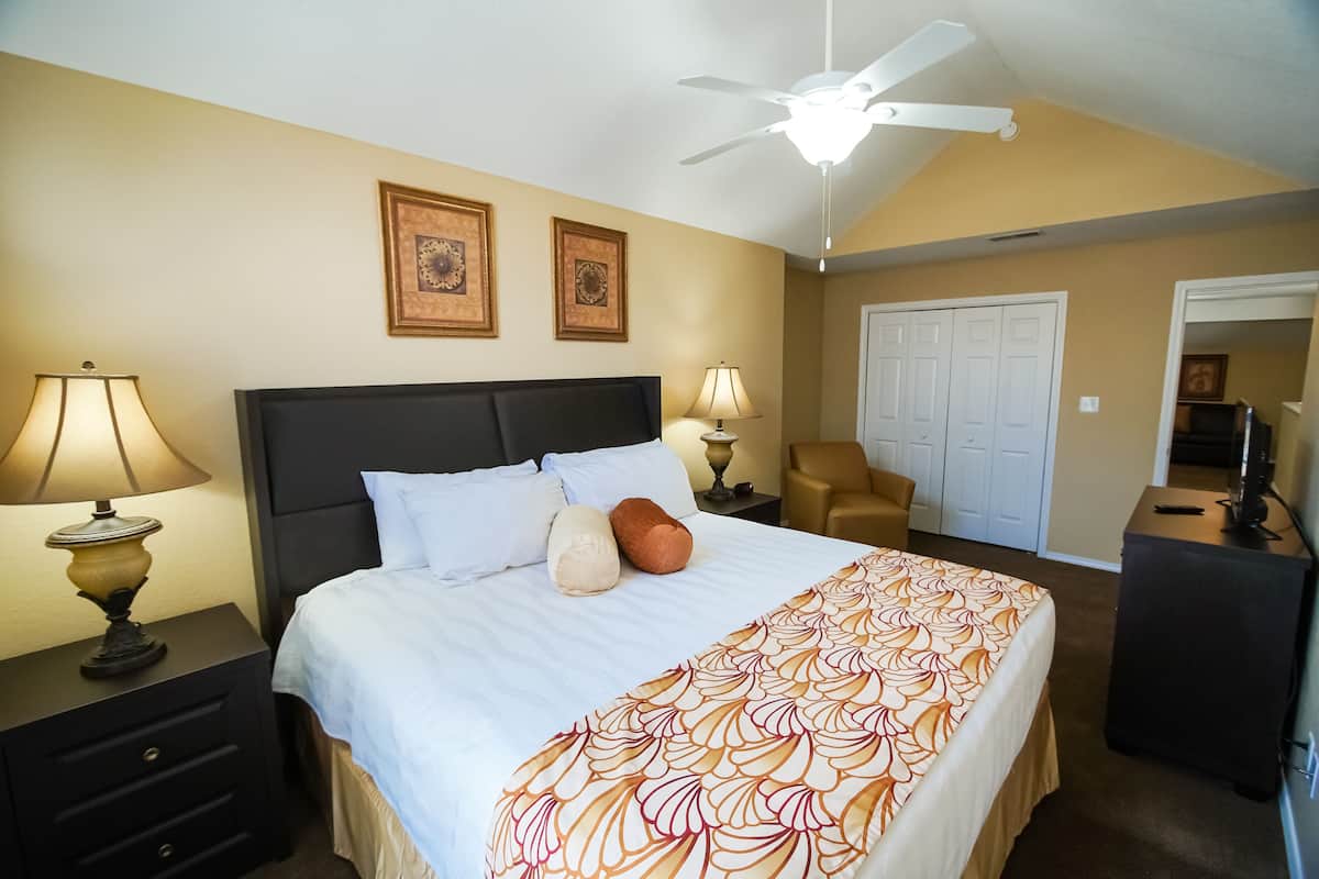 Une chambre d’hôtel comprenant un lit, deux lampes de chevet, un ventilateur de plafond, une chaise, une armoire et un téléviseur.