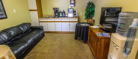 A living room with a black leather couch, a wooden cabinet, a water dispenser, a television, and a small table with a plant.