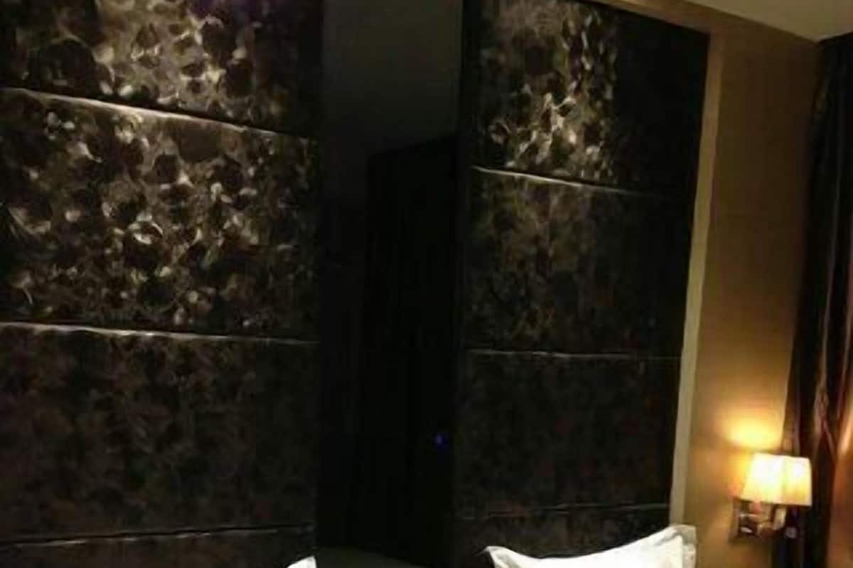 Una habitación de hotel con dos camas, un cabecero de textura oscura y una mesita de noche con lámpara.