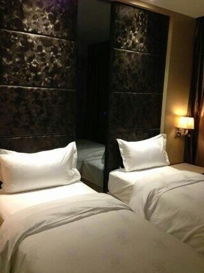 Ein Hotelzimmer mit zwei Betten, einem dunklen, strukturierten Kopfteil und einem Nachttisch mit Lampe.