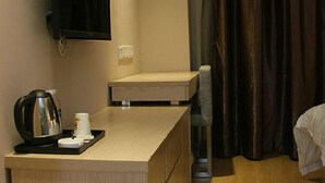 Habitación de hotel con un escritorio de madera, cafetera, televisor y cama con cortina.