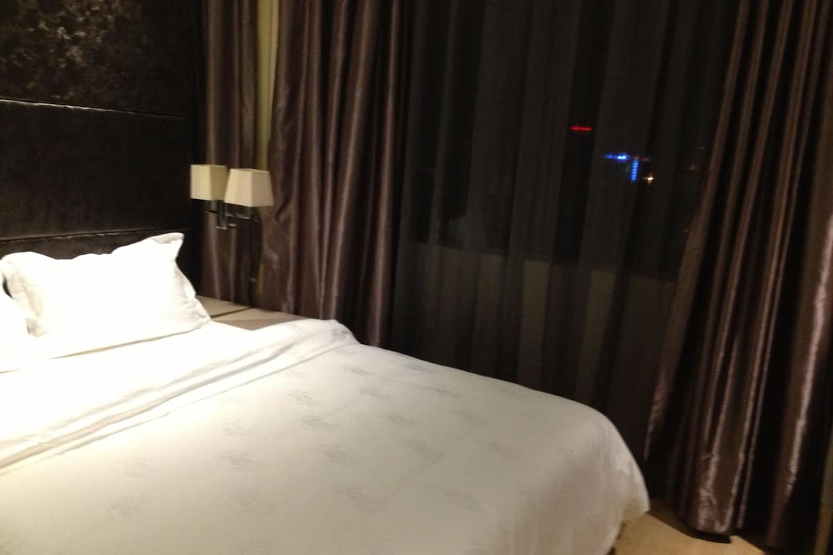 Habitación de hotel con cama, mesita de noche, lámpara y vistas a través de una ventana con cortinas.
