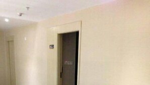 Un pasillo con barandilla de vidrio, alfombra estampada con motivos de hojas y una puerta con un cartel.
