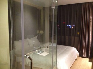 A modern hotel room with a glass partition, a bed with white linens, a bedside table, and a lamp. - Super 8 Hotel Guangdong University of Foreign Studies (Guangzhou)