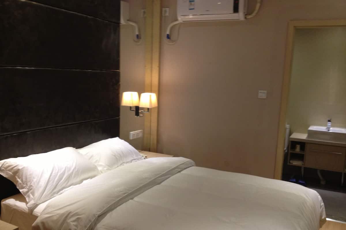 Habitación de hotel con cama, lámparas de noche, aire acondicionado en la pared y baño con lavabo y espejo.