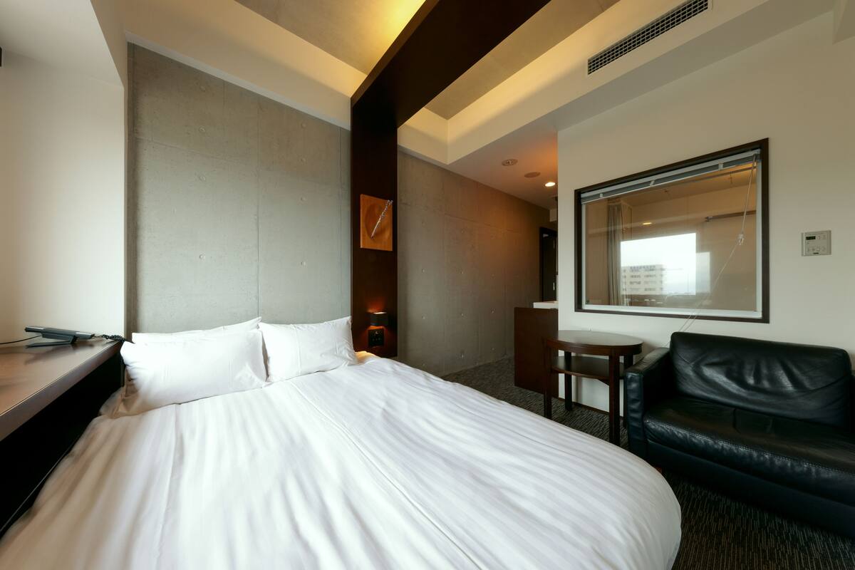 A hotel room with a large bed, a desk, a chair, a leather sofa, and a mirror on the wall.