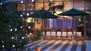An outdoor dining area with tables and chairs, umbrellas, and a decorative light wall in the background.