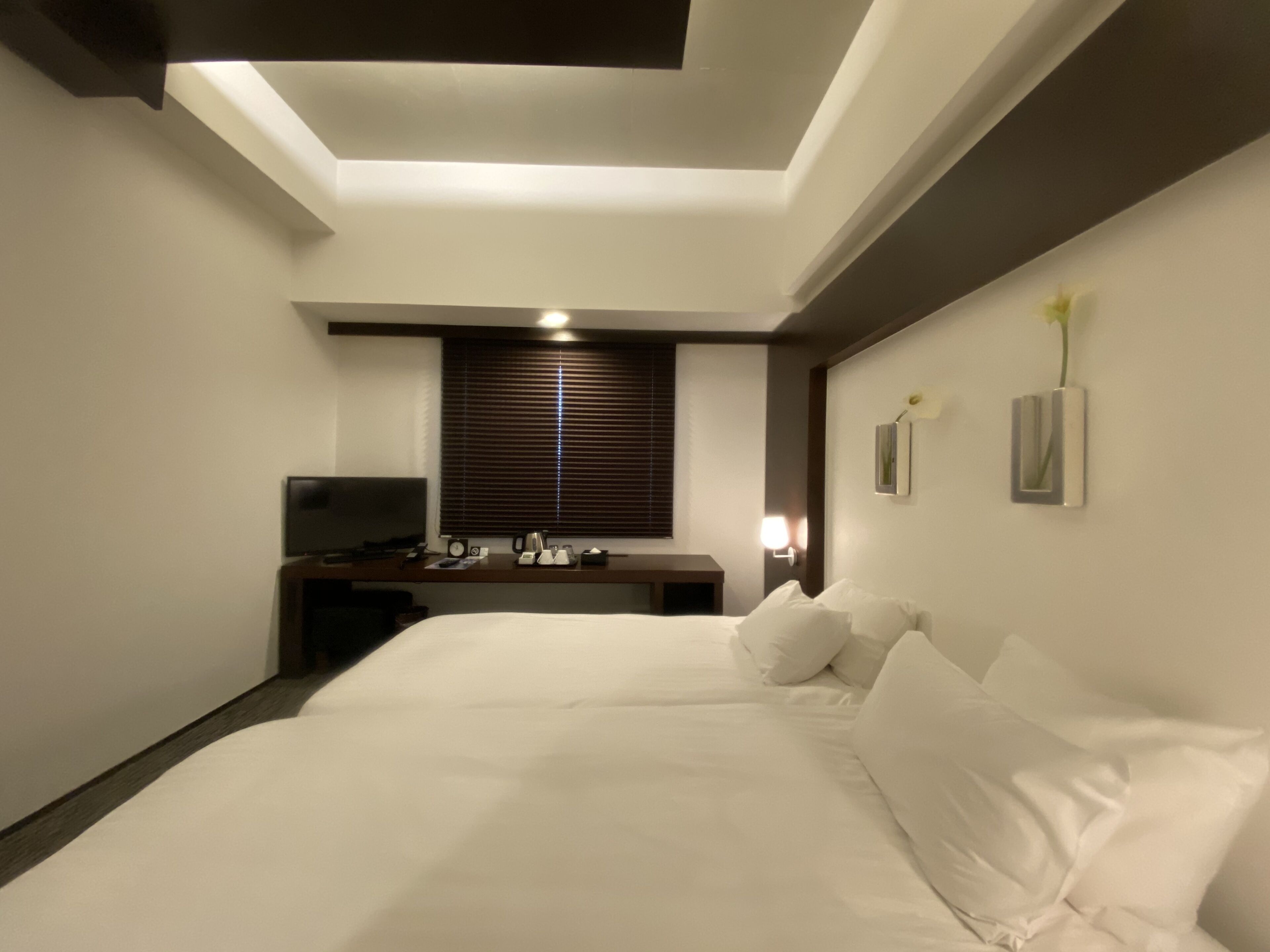 Habitación de hotel con una cama grande, un escritorio con silla, un televisor y una ventana con persianas.