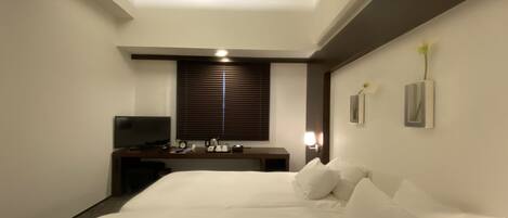 Habitación de hotel con una cama grande, un escritorio con silla, un televisor y una ventana con persianas.