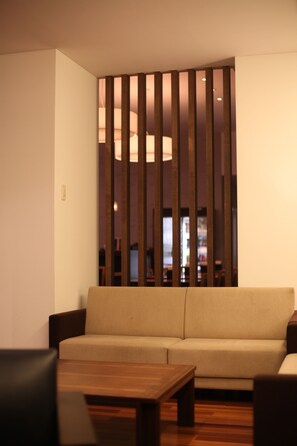 A modern living room with a sofa, a wooden coffee table, and a partition with vertical slats. - Furano Natulux Hotel (Furano)