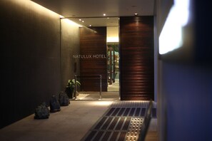 The entrance to the Natulux Hotel with a modern design, featuring a glass door and a metal barrier. - Furano Natulux Hotel (Furano)
