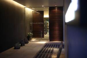 The entrance to the Natulux Hotel with a modern design, featuring a glass door and a metal barrier.