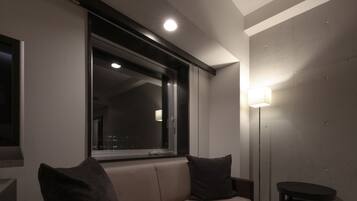 Una sala de estar moderna con un sofá beige, dos cojines oscuros, una lámpara de pie y una mesita.