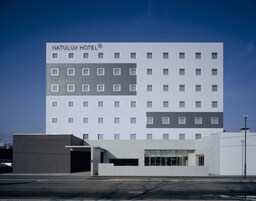 A modern hotel building with a flat facade, multiple windows, and a sign reading "NATULUX HOTEL".
