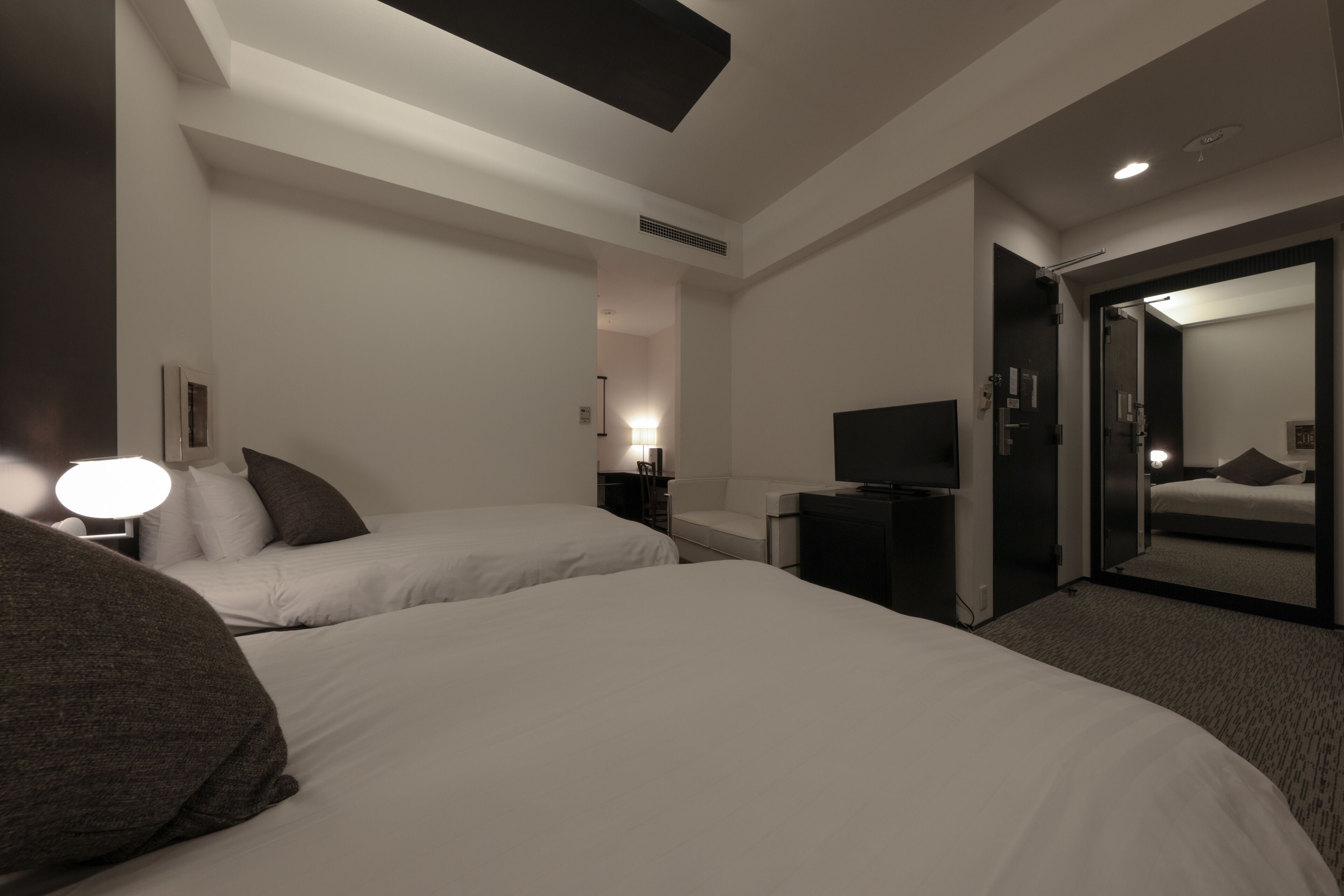A hotel room with two beds, a TV, a desk, and a mirror.