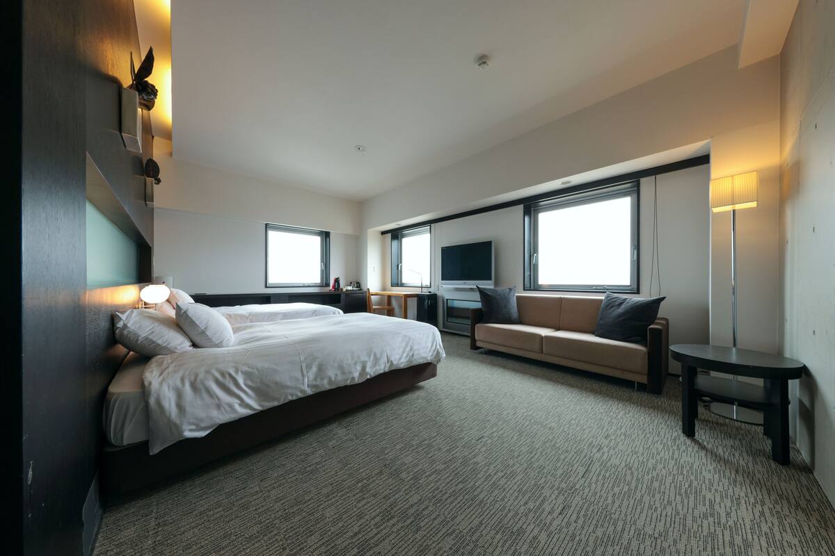 A modern hotel room with a large bed, a sofa, a TV, and a desk.
