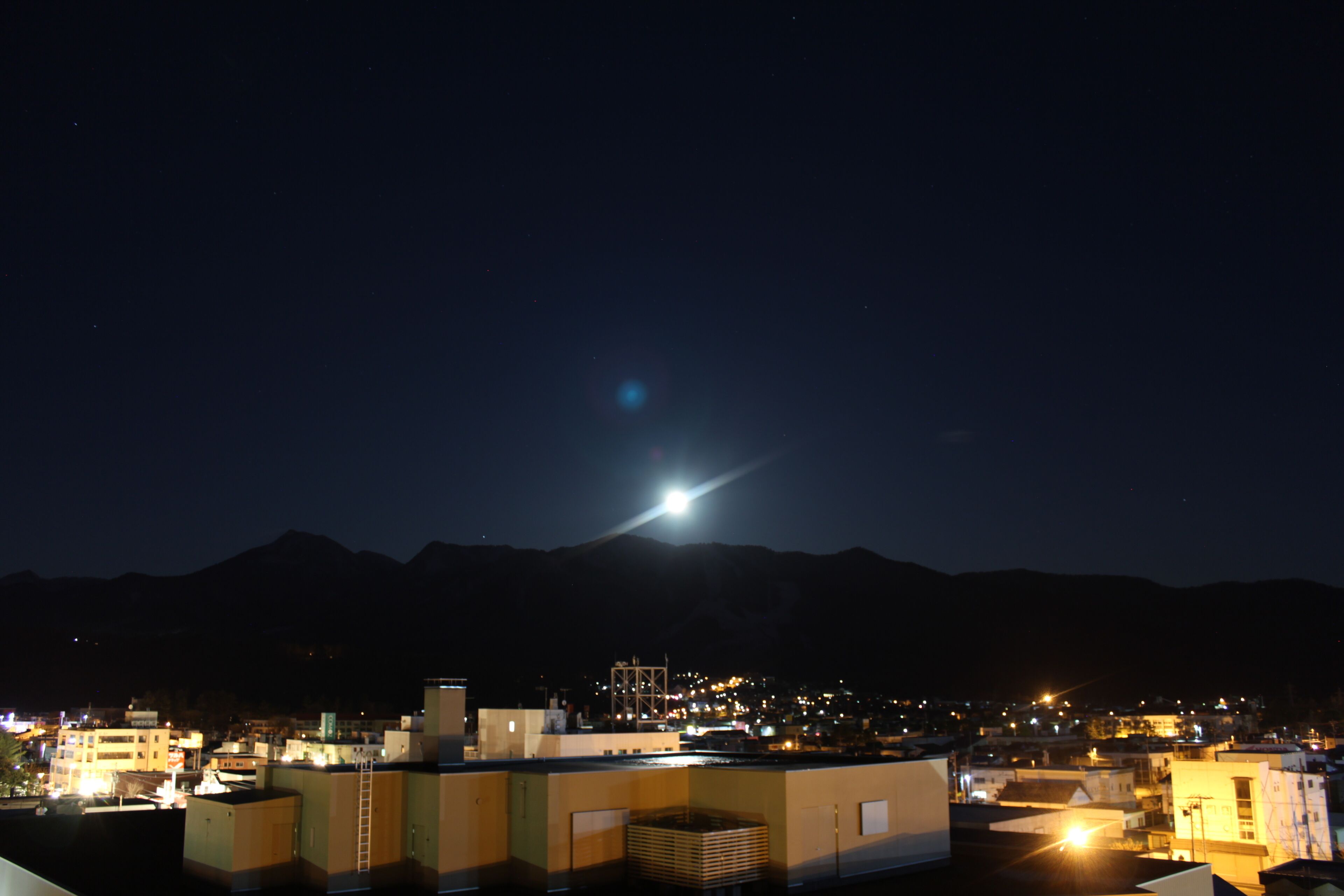 Un paisaje urbano nocturno con una montaña al fondo y una luna brillante en el cielo.
