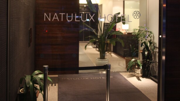 A hotel entrance with a glass door, a reception desk, and potted plants.