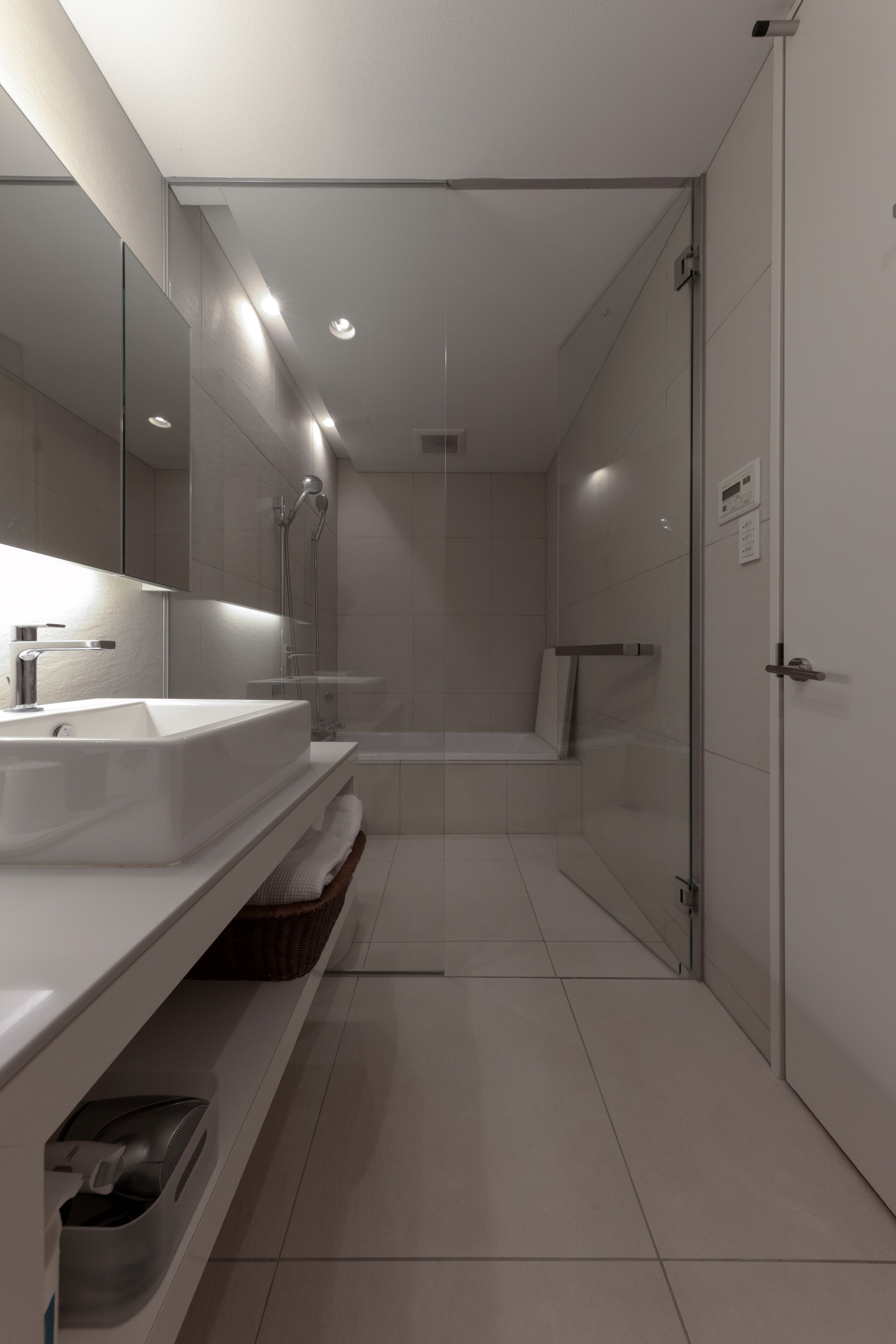 Un baño moderno con un espejo grande, un lavamanos, una ducha y un inodoro con mampara de vidrio.