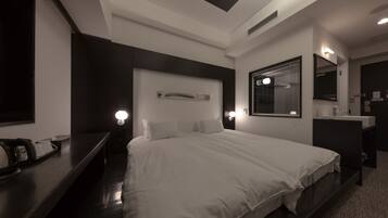 Une chambre d’hôtel moderne avec un grand lit, des tables de chevet, un miroir et une petite étagère ornée d’objets décoratifs.