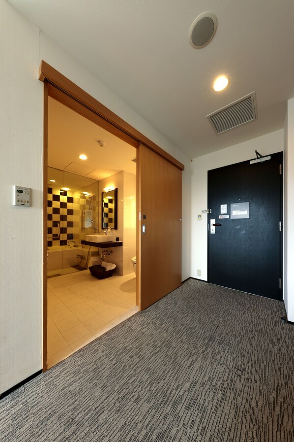 Habitación de hotel con piso a cuadros, una puerta negra y un baño con espejo y lavamanos.