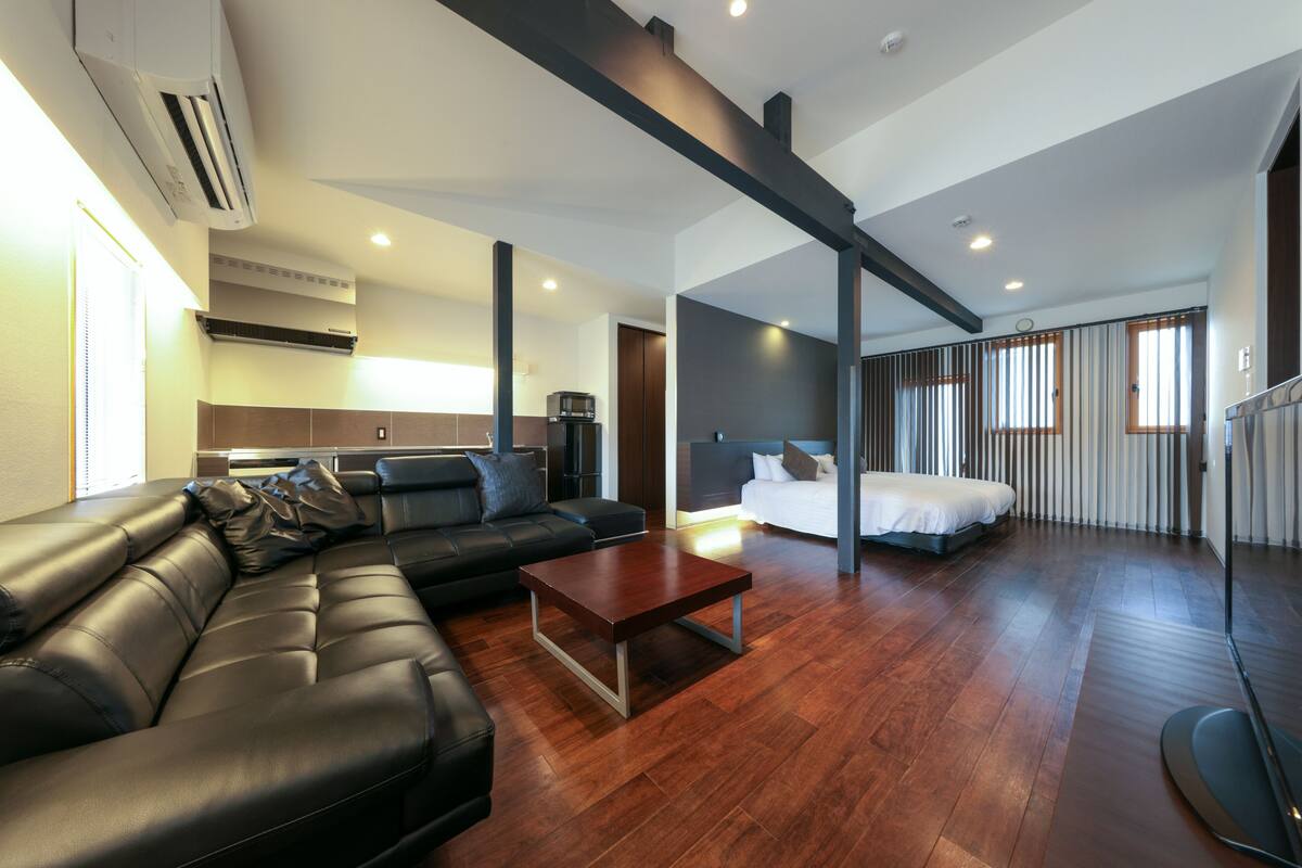 A modern living room with a leather sofa, a wooden coffee table, and a bed with a white mattress.