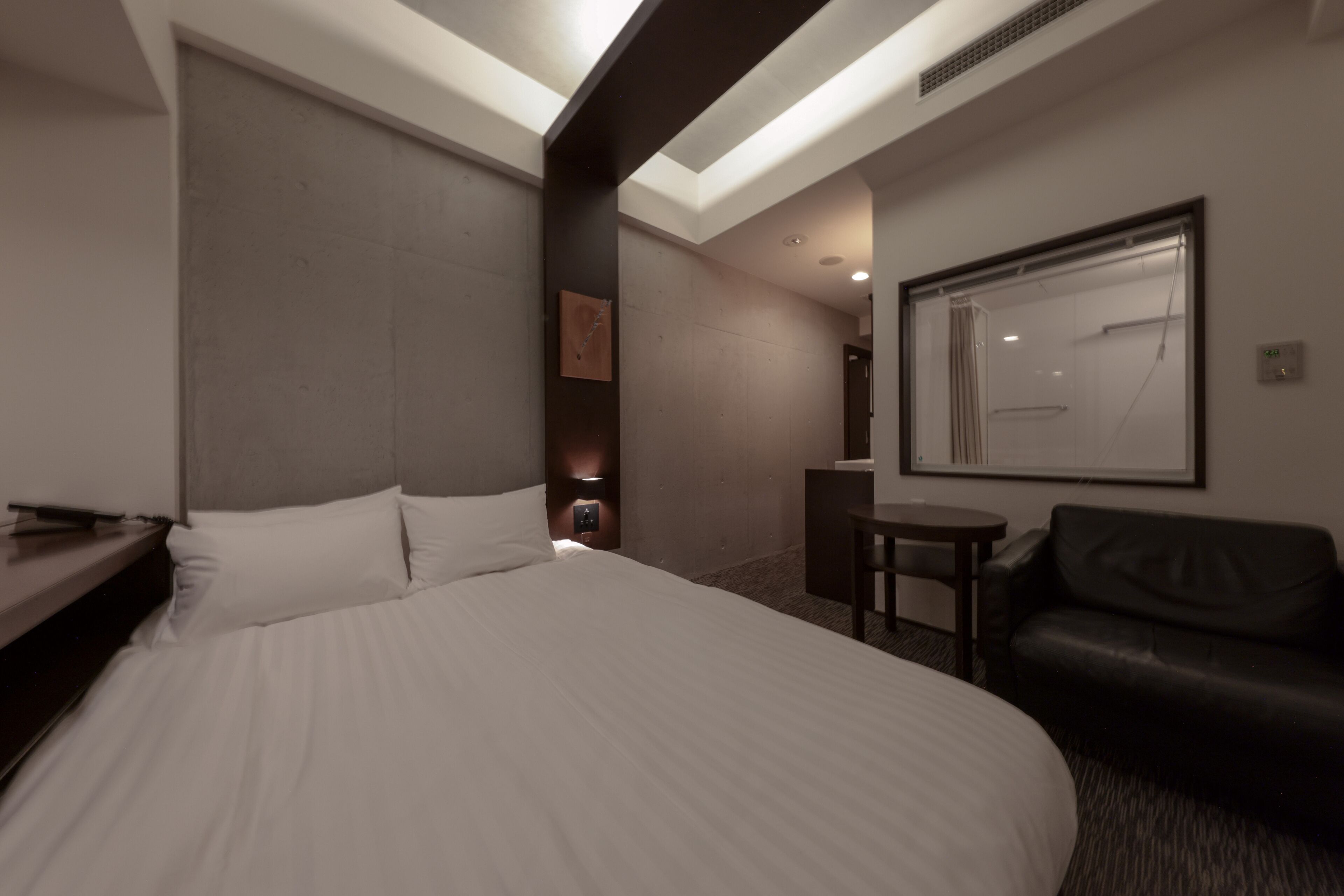 A modern hotel room with a large bed, a small desk, a chair, and a mirror on the wall.