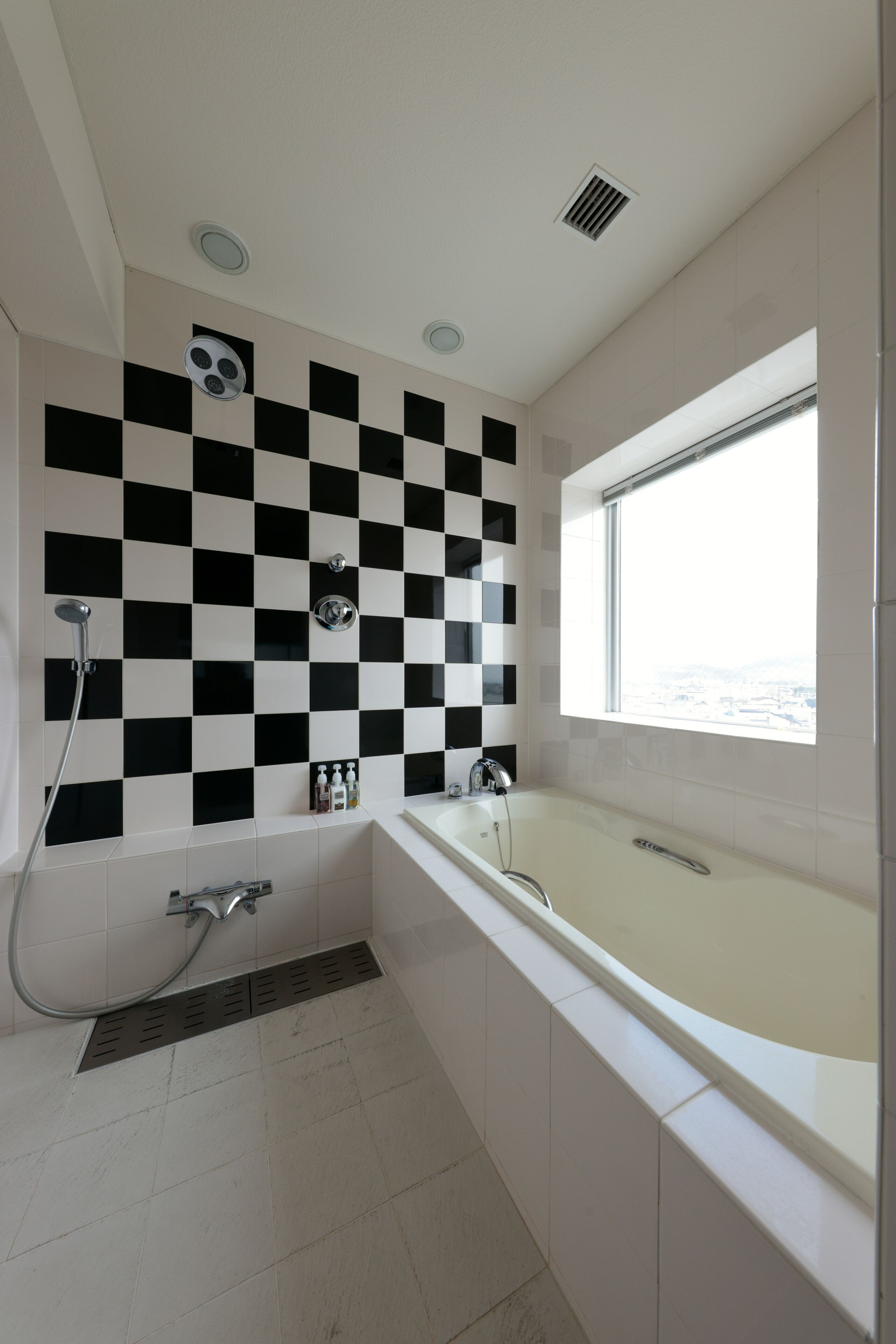 Une salle de bain moderne avec un mur recouvert de carreaux noirs et blancs formant un motif à carreaux, une baignoire, une douche et une fenêtre offrant une vue.