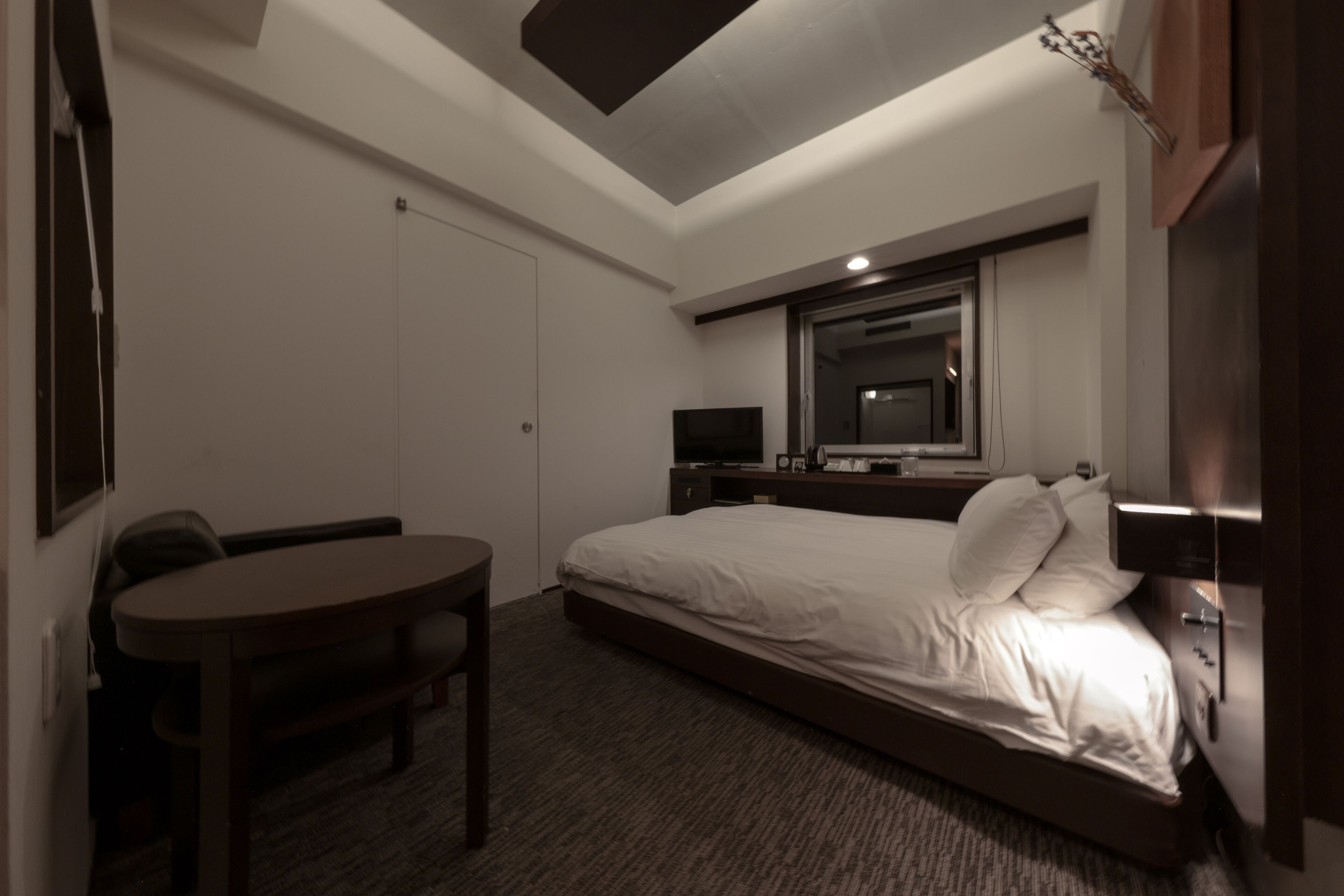 Habitación de hotel con cama, escritorio, silla, televisor y espejo.
