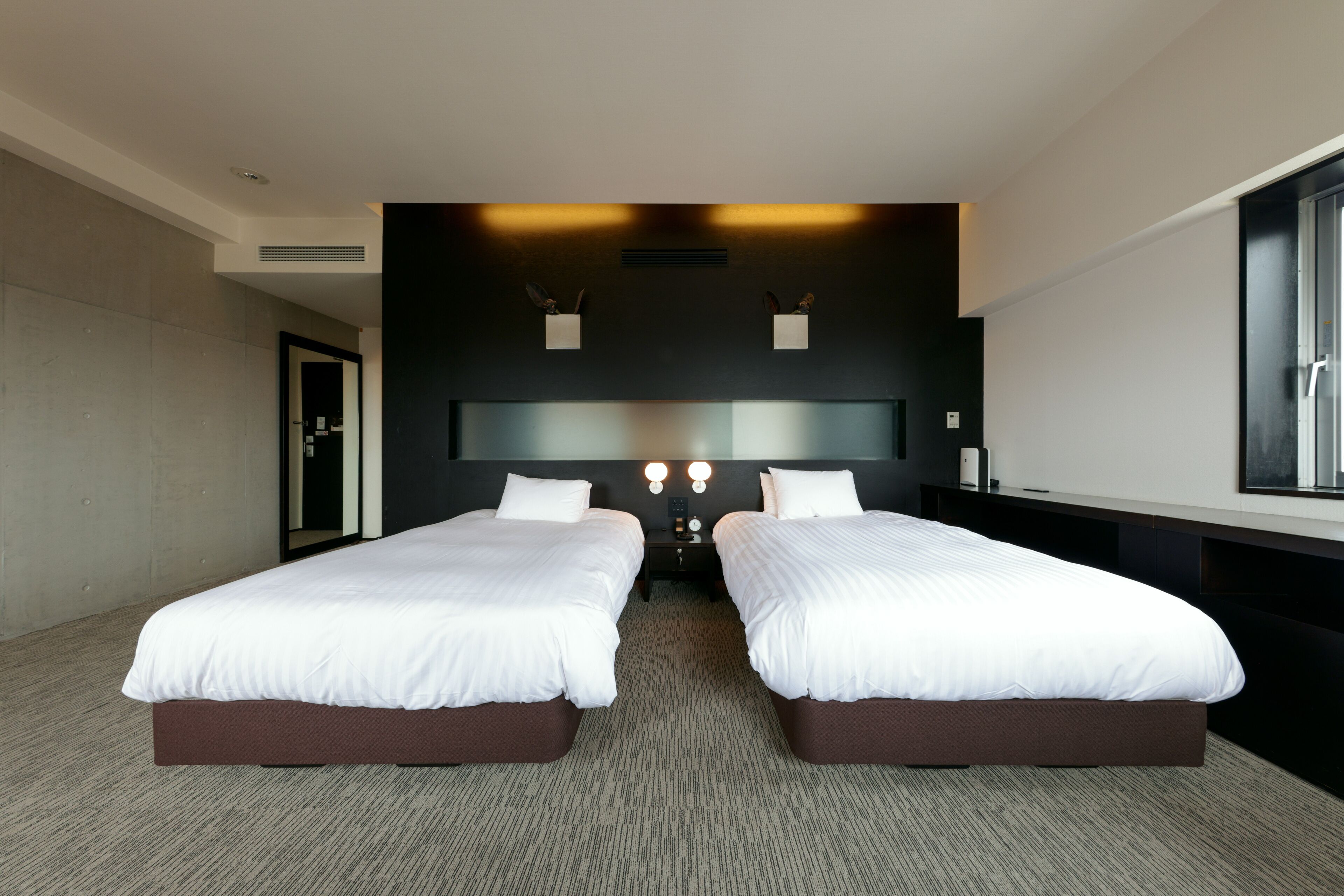 Una habitación de hotel moderna con dos camas, un espejo grande y vistas a la ciudad.