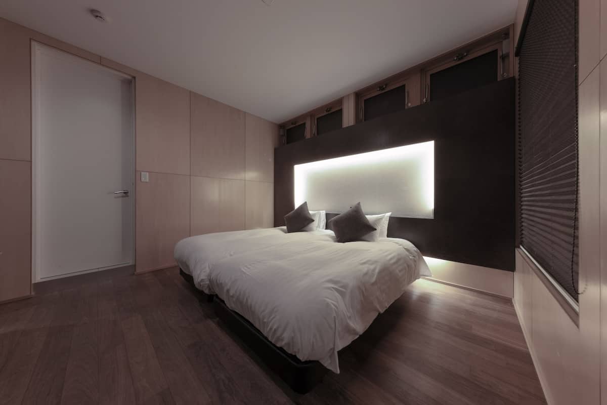 A modern bedroom with a large bed, built-in headboard, and a wardrobe.