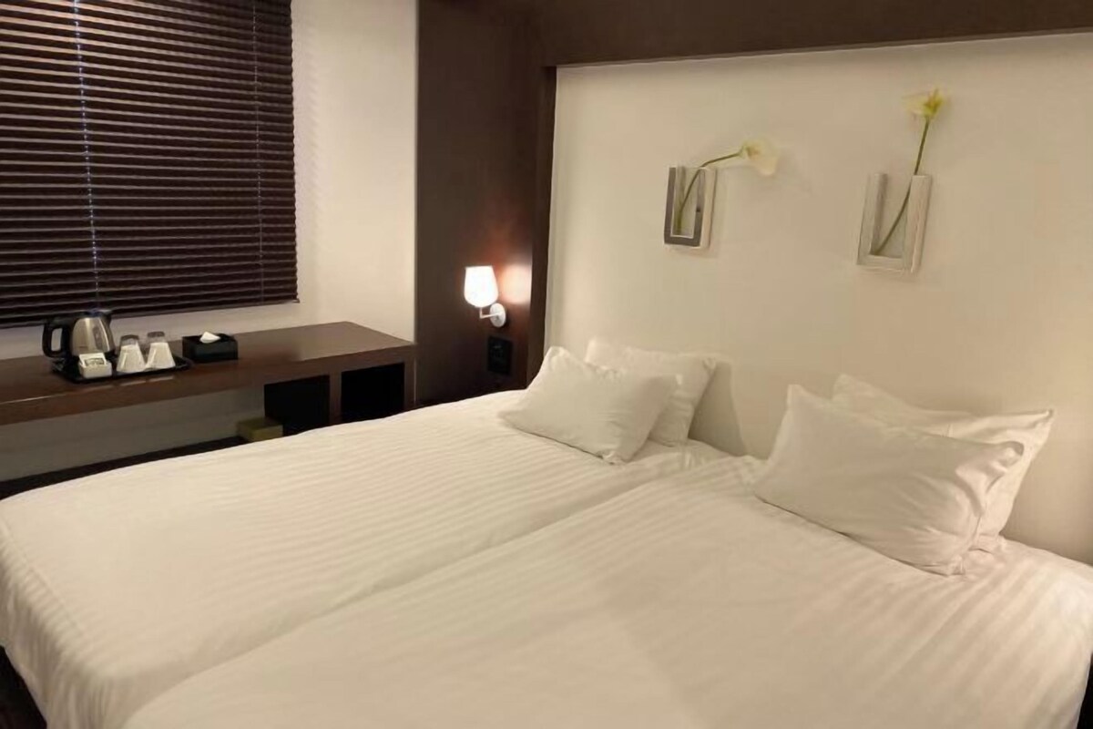 Une chambre d’hôtel avec un grand lit, une table de chevet avec une machine à café et une lampe fixée au mur.