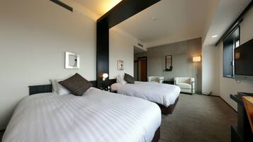 A hotel room with two beds, a desk, a chair, a TV, and a lamp.
