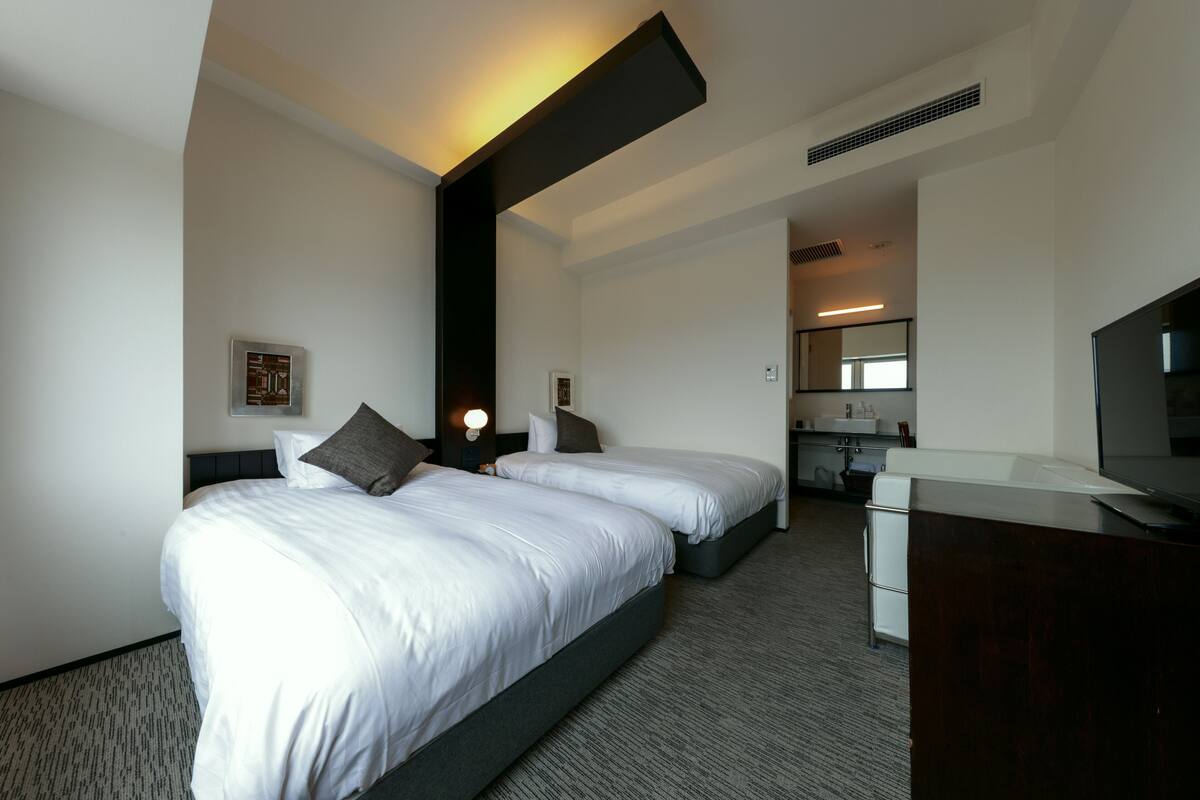 A hotel room with two beds, a desk, a mirror, and a television.