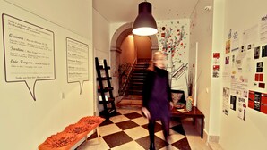 A hotel corridor with a checkered floor, a bench, a staircase, and various wall decorations including menus and posters. - Hall Chiado (Lisbon)